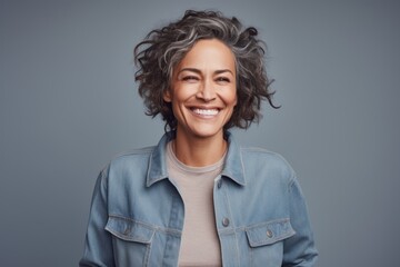 Portrait of a smiling woman in her 50s sporting a rugged denim jacket against a pastel or soft...