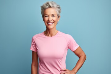 Portrait of a smiling woman in her 70s wearing a moisture-wicking running shirt against a pastel or...