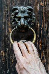 Palermo, Sicily, Italy  A woman's hand  uses a lion shaped door knocker on a wooden door.