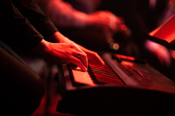 Hands of a musician playing a synthesizer in the red stage light
