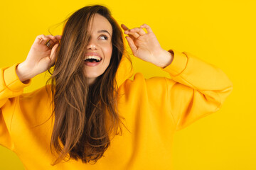 Close up photo of trendy cheerful cute nice sweet youngster laughing looking away toothy wearing hood isolated over yellow color background. Funny girl look playful holding hood.