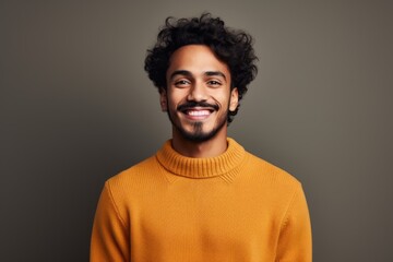 Obraz premium Portrait of a cheerful indian man in his 20s wearing a cozy sweater against a minimalist or empty room background. AI Generation