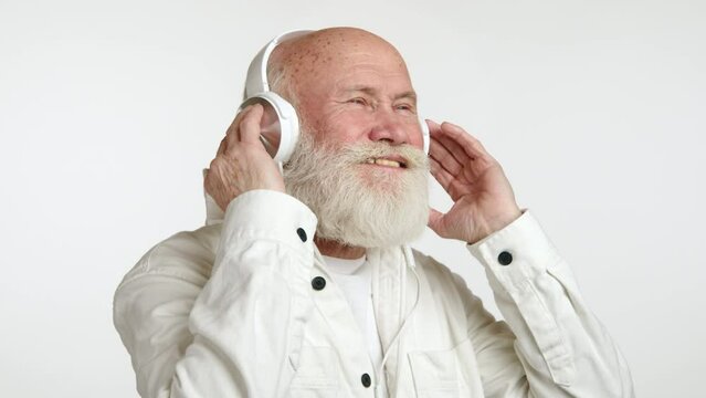 A gleeful individual is basking in the auditory experience, gently adjusting his headphones, clad in a casual white top, his demeanor exuding musical 