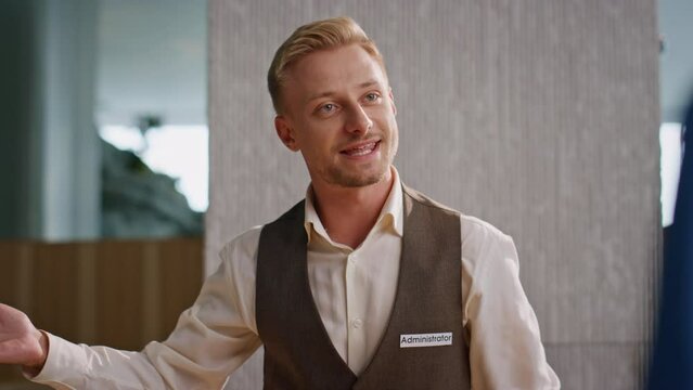 Friendly concierge talking guests at reception closeup. Smiling man in uniform