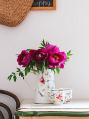 Purple peonies in a jug and cups on a table. Beautiful spring morning scene