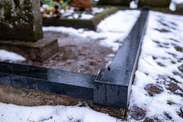 granite grave place borders in graveyard. Ground is covered with melting snow. Latvia traditional cemetery culture.