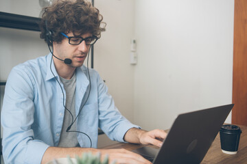 Male agent or telemarketing in eyeglasses with headphone talking to customer working at home. Man meeting video call work remotely on weekend. Teacher teaching or consulting online.