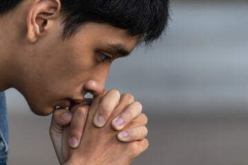 A man praying and close your eyes in praying. Prayer to pray. A young man is holding palms by his lips, whispering a prayer, and asking. - obrazy, fototapety, plakaty