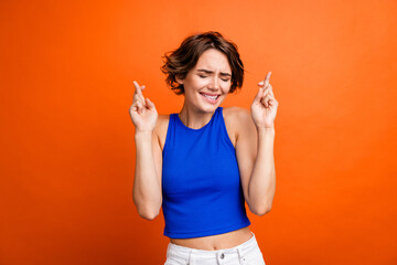 Portrait of pretty worried person closed eyes biting lips crossed fingers isolated on bright orange color background