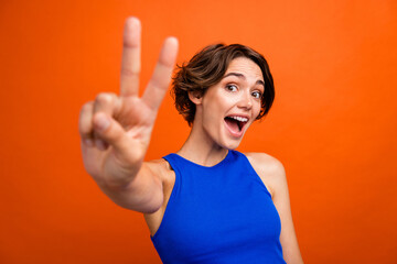 Photo of nice cheerful impressed person open mouth arm fingers demonstrate v-sign isolated on orange color background