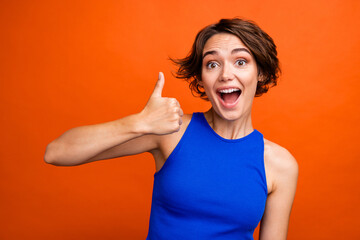 Portrait of pretty impressed person open mouth arm finger demonstrate thumb up isolated on orange color background