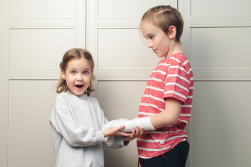 Child girl holding his brother's broken arm. Boy holds hand bent broken arm cast on his arm. Girl is in shock.