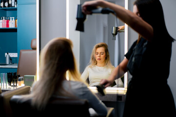 the hairdresser dries the client's wet hair with a hair dryer in the beauty salon, a care procedure