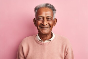 Obraz premium Portrait of a happy indian man in his 80s showing off a thermal merino wool top against a solid pastel color wall. AI Generation