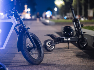electric bike and a scooter are parked in the park at night. Modern urban transport