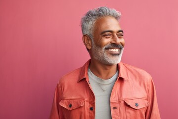 Portrait of a blissful indian man in his 60s sporting a rugged denim jacket against a solid pastel...
