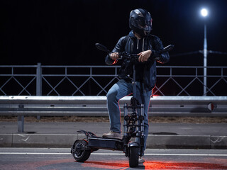 A man in a helmet poses on an electric scooter on a night road. Modern stylish and powerful urban transport.
