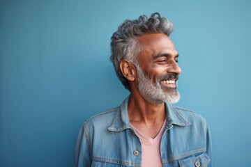 Portrait of a blissful indian man in his 60s sporting a rugged denim jacket against a solid pastel...