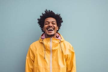 Portrait of a happy afro-american man in his 20s sporting a waterproof rain jacket against a solid...