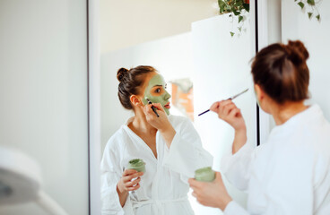 Young woman applying clay mask on face