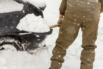 A man with a shovel in his hands removes snow around the car.