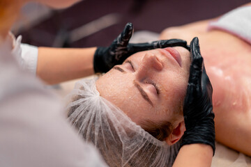 close-up beautician in gloves rubs the serum with massage movements on the face of a client in salon