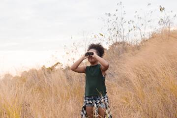 A thoughtful young girl stands amidst a wheat field, holding a camera, capturing the serene beauty of the natural surroundings during the golden hour. African American kid happy traveling in nature