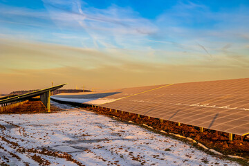 Ein Solarpark mit vereisten und schneebedeckten Photovoltaik Modulen während des Sonnenaufgangs.