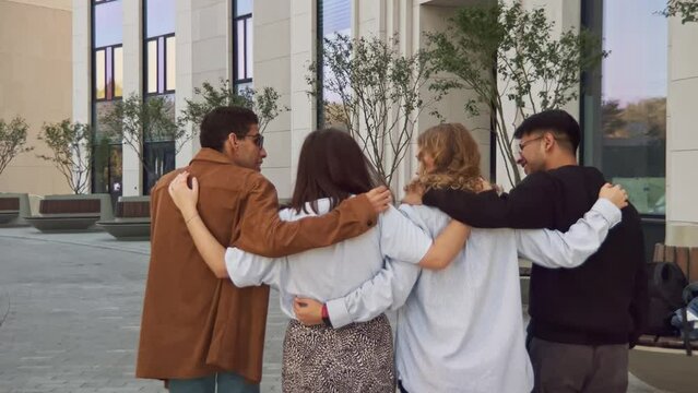 Group of positive multi race diverse classmates walking after college exams, celebrate, hug each other, talk with joy, happy and positive emotions. Friendship, students after lesson. Back view
