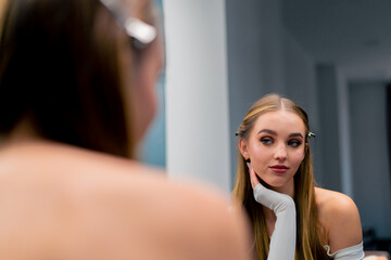 satisfied smiling girl looks at herself in the mirror evaluates the evening make-up in beauty salon