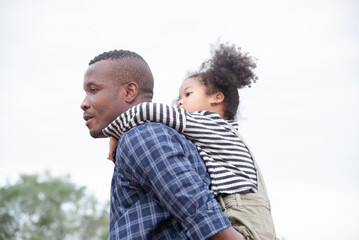 Happy African American family with adorable children in weekend vacation camping outdoors in countryside, father carry daughter on shoulder walking around in forest with fun, bonding relationship
