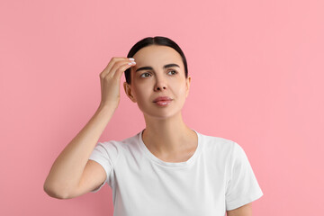 Woman with dry skin checking her face on pink background