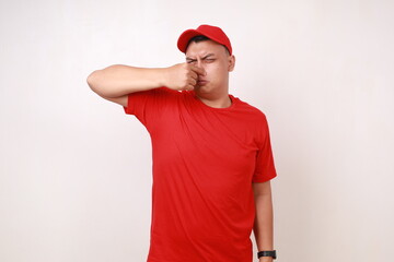 Funny young asian courier covering his nose, bad smell concept. Isolated on white