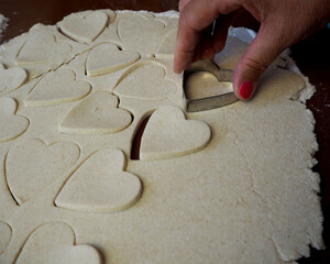 On a brown silicone mat, gluten free cookies are squeezed into a heart shape from raw rolled out dough with cottage cheese. side view of sweet pastries at home