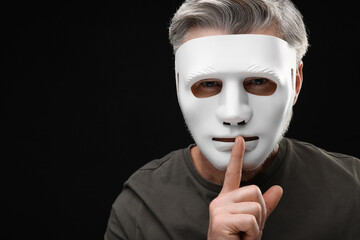 Man in mask showing hush gesture against black background. Space for text