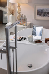 White wooden tray with tablet, cassette player and burning candles on bathtub in bathroom