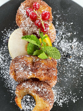 Apple Fritters on a dark plate with sugar and fruits