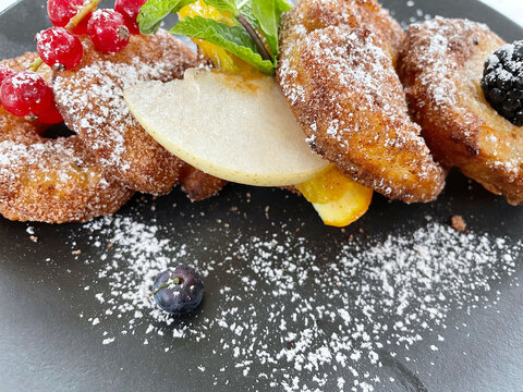 Apple Fritters on a dark plate with sugar and fruits