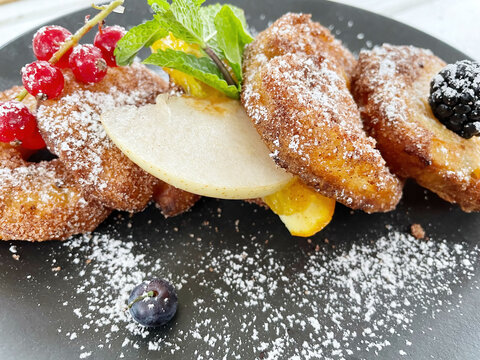 Apple Fritters on a dark plate with sugar and fruits