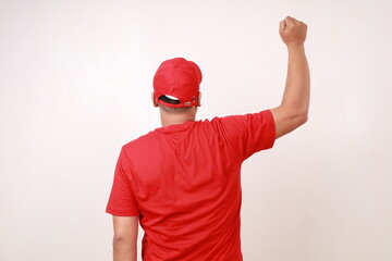 Back view of Asian delivery guy employee man in red standing while lifting clenched hand, isolated on white background