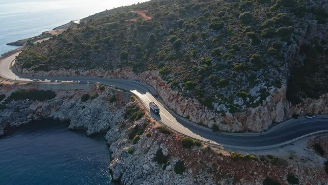 Dump truck driving on winding coastal road along the coast of Mediterranean sea, Logistic and shipping construction materials to coastal town, Aerial view