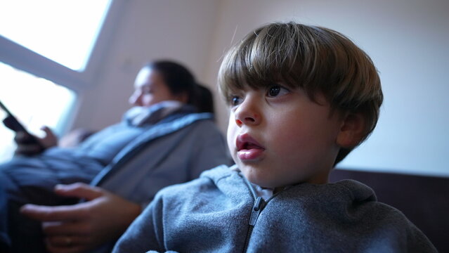 Closeup Of Little Boy Staring At Entertainment Media Off-camera. Hypnotized Child Watching Cartoons At Home Seated On Couch Sofa