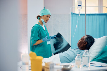 Female doctor talks to black senior patient after examining his X-ray image in hospital.