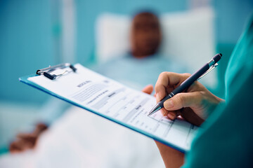 Close up of nurse taking notes in patient's medical record during his recovery in hospital.