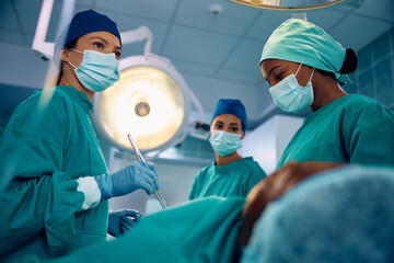 Team of female surgeons preforming surgical procedure in operating room at medical clinic. - obrazy, fototapety, plakaty