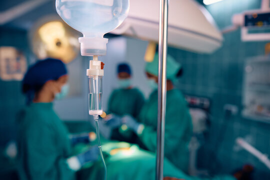 Close up of IV drip with surgical intervention in background.