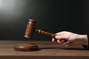 Judge striking mallet at wooden table against dark background, closeup