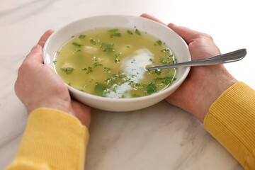 Man with bowl of delicious chicken soup at light marble table, closeup