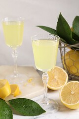 Tasty limoncello liqueur, lemons and green leaves on table