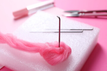 Felting mat, needles and wool on pink background, closeup